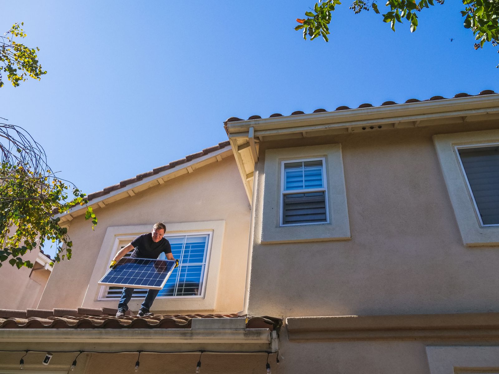 Installer carrying a solar panel across a tiled home rooftop