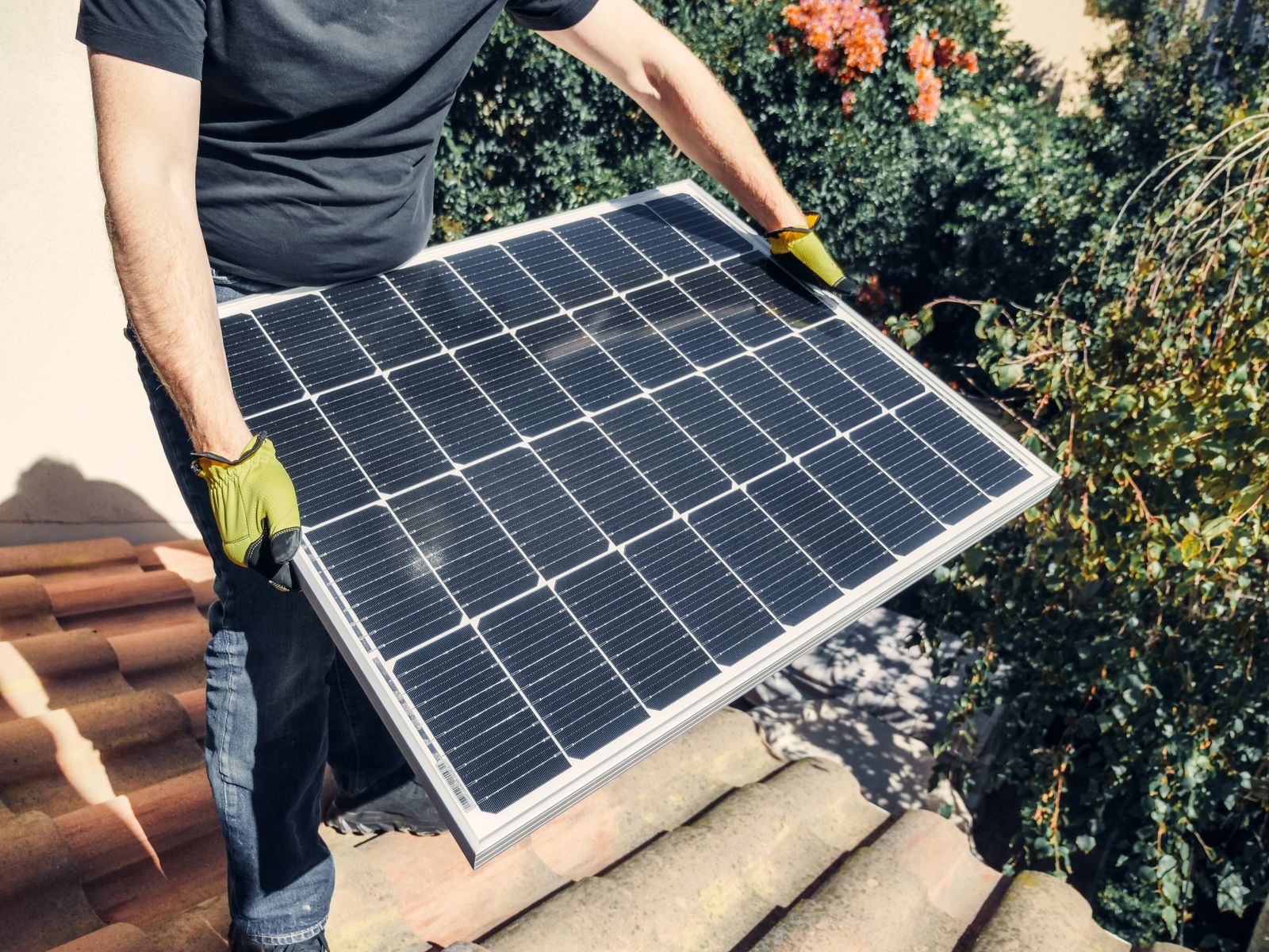 Installer carrying a solar panel over a tiled roof